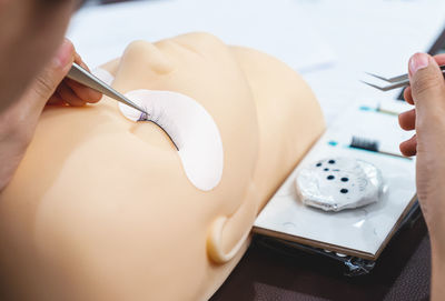 Cropped hand of beautician making false eyelash on mannequin