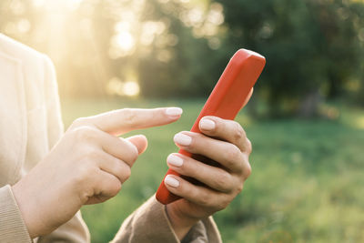 Closeup of female hands using a smart phone, nature background. woman using red mobile phone