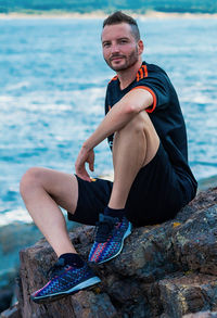 Portrait of young man sitting on rock by sea