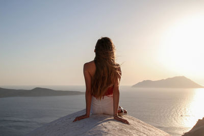 Girl dressed in white and red sitting on the roof of white church overlooking the mediterranean sea