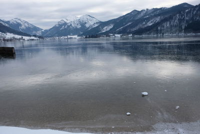 Scenic view of frozen lake by snowcapped mountains against sky