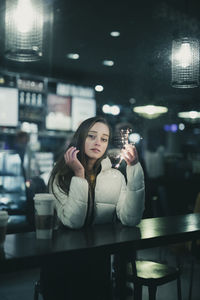 Portrait of young woman holding illuminated string light at restaurant