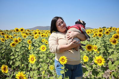 Portrait of beautiful woman with dog standing by sunflower field against clear sky