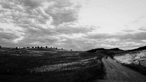 Road passing through field against cloudy sky