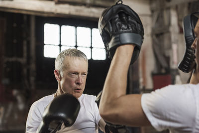 Determined senior male boxer practicing with friend in gym