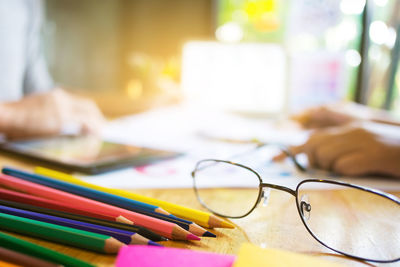 Close-up of colored pencils by eyeglasses on desk at office