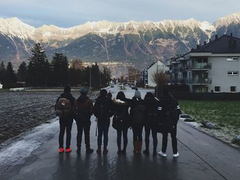 Full length rear view of friends standing on wet road against mountains