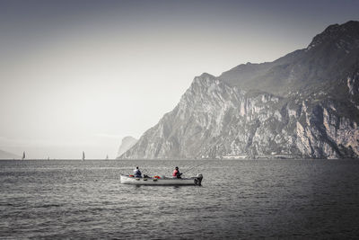 People fishing in sea by mountains against sky