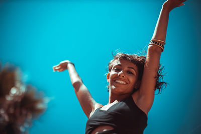 Low angle portrait of cheerful woman against clear blue sky