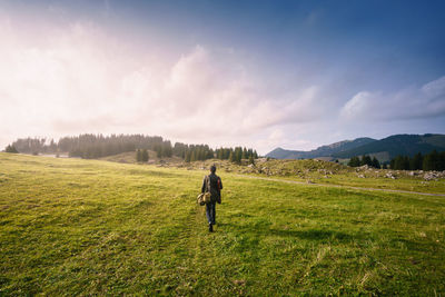 Rear view of man walking on field against sky