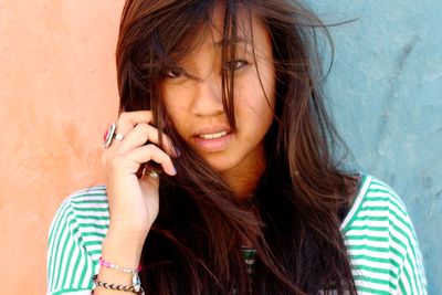 Close-up portrait of young woman with tousled hair against wall