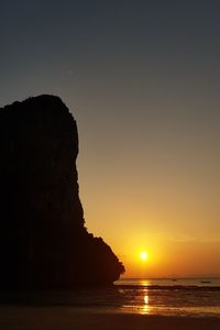 Silhouette rocks on sea against sky during sunset