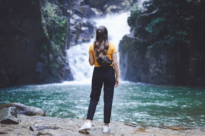 Rear view of woman standing on rock against waterfall