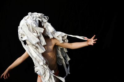 Shirtless boy standing with white fabrics against black background