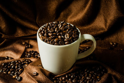 Close-up of roasted coffee beans with cup on fabric
