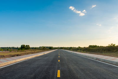 Road passing through field against sky