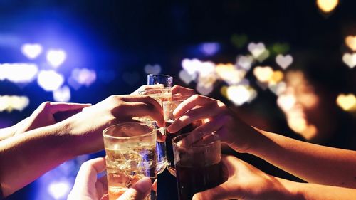 Cropped hands of men and women holding beer glasses at night