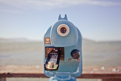 Blue coin-operated binocular at sea shore against sky