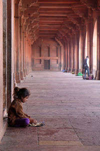 Rear view of girl sitting on footpath against building