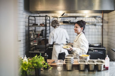 Side view of waitress carrying food plates in kitchen at restaurant