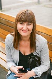 Portrait of smiling woman using mobile phone while sitting on bench