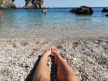 Low section of person on rock at beach against sky