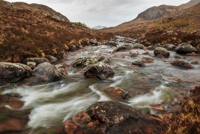 Stream flowing through rocks in mountains against sky