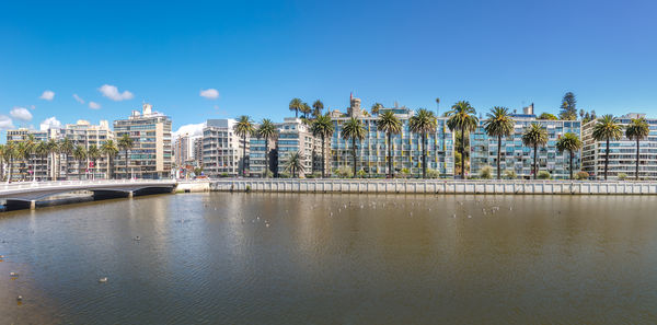 Buildings by river against clear blue sky