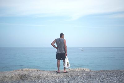 Rear view of man standing on beach against sky