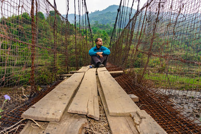 Man sitting alone at vintage iron suspension bridge from low angle