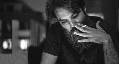 Close-up of mid adult bearded man smoking cigarette at home