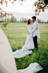 Romantic bride and groom on field against sky