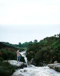 Woman standing on rock by sea against clear sky