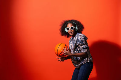 Young woman wearing sunglasses standing against red background