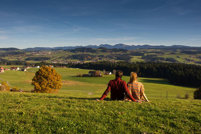 Rear view of people sitting on agricultural field against sky