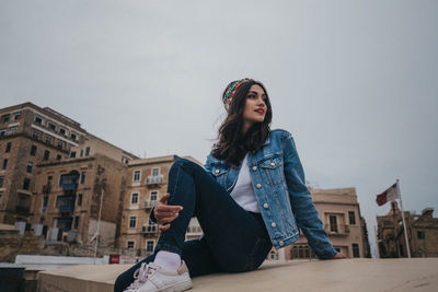 Portrait of beautiful young woman sitting against sky