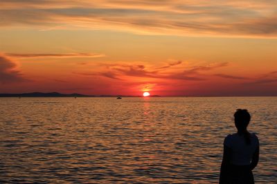 Rear view of man standing by sea against orange sky