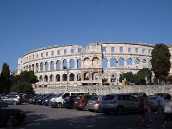 Cars parked by pula arena against clear blue sky