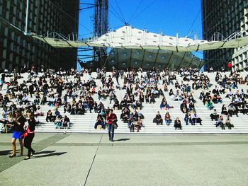 Crowd sitting on steps amidst buildings in city