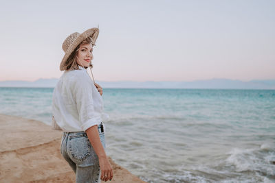 Full length of young woman standing at beach against sky