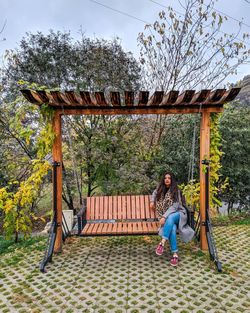 Portrait of woman sitting on seat against trees