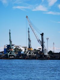 Cranes at harbor against sky