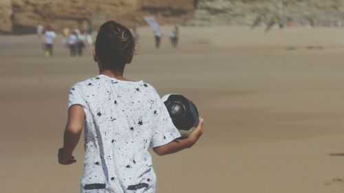 Rear view of woman holding ball while running at beach