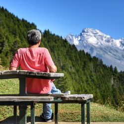 Rear view of man sitting on picnic table against mountain