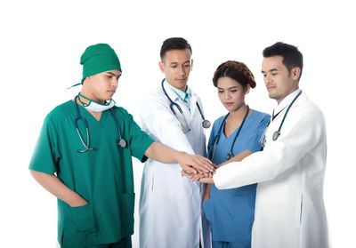 Doctors stacking hands while standing against white background