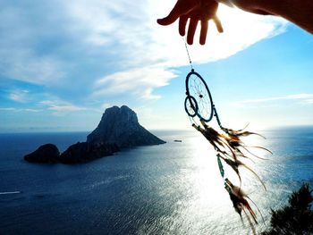 Cropped image of hand holding dream catcher against sea