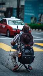 Rear view of man holding umbrella on street in city