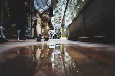 Low section of people walking at footpath reflecting on puddle