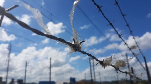 Low angle view of barbed wire with plastic against sky