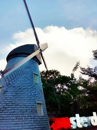 Low angle view of windmill by building against sky